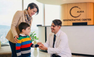 A doctor kneels to talk to a young boy while his mother stands beside him at the reception area of a regenerative center.
